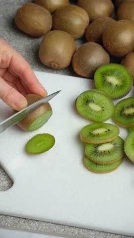 The process of cutting fresh ripe kiwi into slices with a knife.