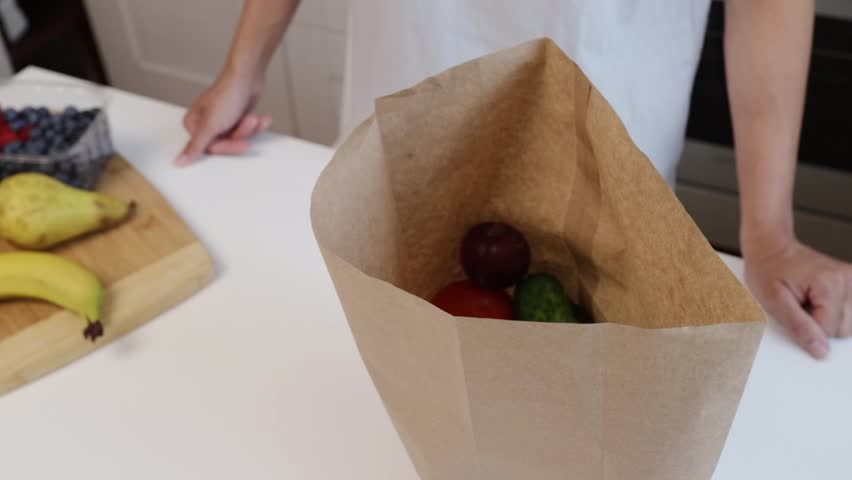 female hands takes fruits and vegetables out of a shopping bag at the kitchen, unpacking groceries, preparation meal, shopping delivery, eating food