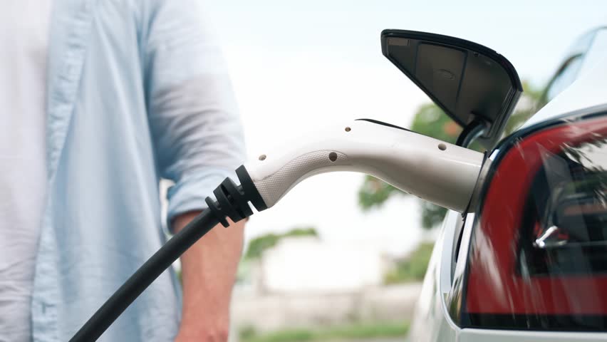 Modern eco-friendly man recharging electric vehicle from home EV charging station. EV car technology utilized for home resident to future environmental sustainability. Fastidious