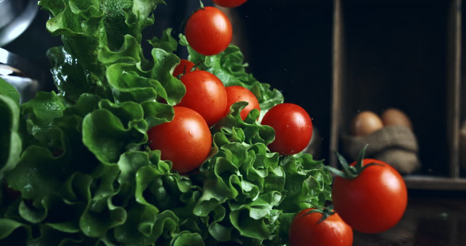 Super Slow Motion Close Up of Fresh Cherry Tomatoes Falling onto Green Lettuce with Water Droplets in a Rustic Kitchen Restaurant Setting at 1000 fps.