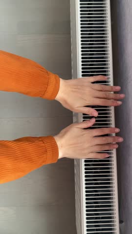 two female hands are warming themselves over a radiator, heating the house