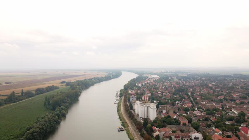 View of serene river winding through countryside near a peaceful town surrounded by fields and greenery in early morning light