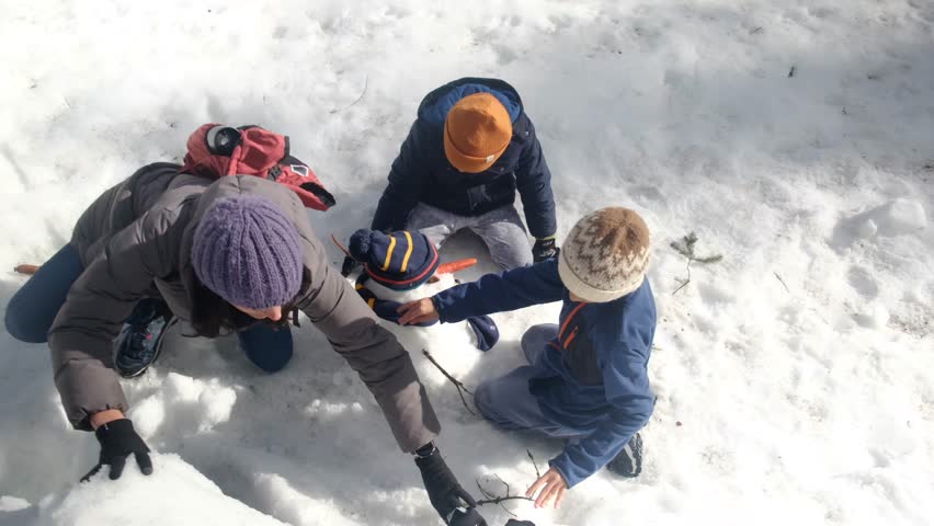 Children building a snowman in a snowy forest. Concept: childhood and winter fun. Bright, natural lighting.