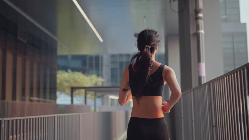 Rear view - Young asian woman runner is training in the summer sunset within a city, The athlete fit and firm girl exercising by jogging workout sport outdoor for her healthy wellness.