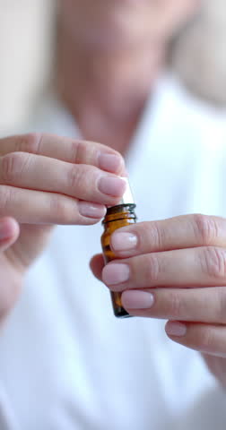 Vertical video: Using dropper bottle, woman applying essential oil at home for skincare. Wellness, aromatherapy, beauty, self-care, natural, routine, slow motion