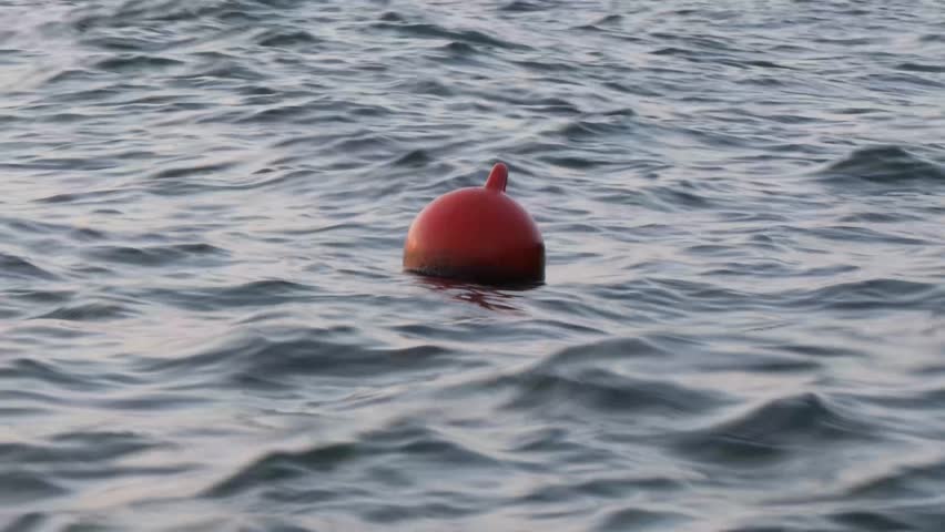 Buoy floating gently on the surface of calm sea water. An orange security buoy drifts on the surface of the sea at dusk. 