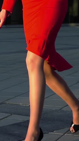 Sexy woman legs in black high heels shoes walking near glass business centre. Steadicam shot. Slow motion. Red suit, spectacles. Cinematic teal and orange sunrise shooting. Vertical Shot.