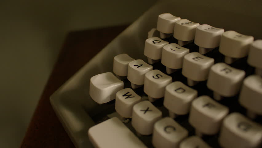 Close-up of a vintage typewriter keyboard with white keys featuring black text and symbols. The layout includes numbers, letters, and punctuation, red key and wide white space bar