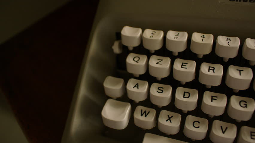 Panning shot of a vintage typewriter keyboard with white keys featuring black text and symbols. The layout includes numbers, letters, and punctuation, red key and wide white space bar