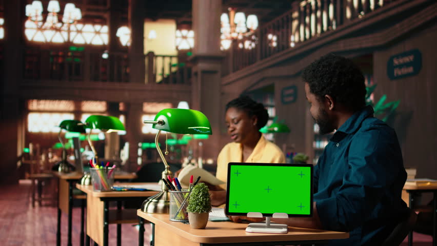 African american students consulting research papers next to green screen from the academic database, learning information from copy books. Young team of pupils at the library. Camera A.