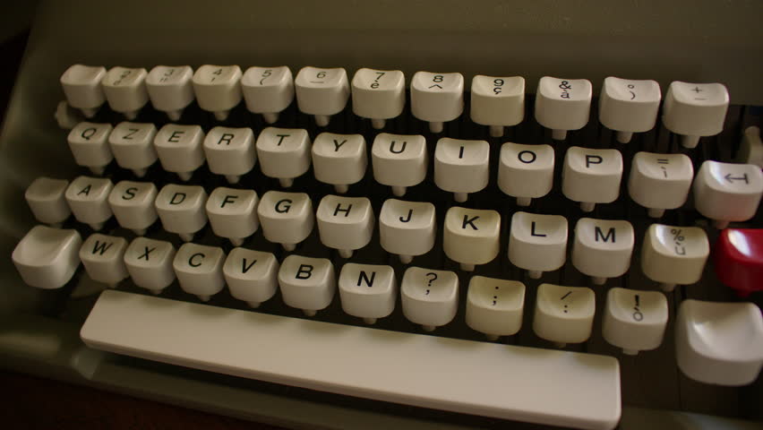 Top down view of a vintage typewriter keyboard with white keys featuring black text and symbols. The layout includes numbers, letters, and punctuation, red key and wide white space bar