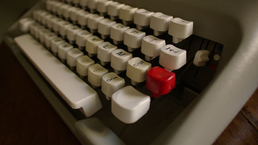 Panning shot of a vintage typewriter keyboard with white keys featuring black text and symbols. The layout includes numbers, letters, and punctuation, red key and wide white space bar