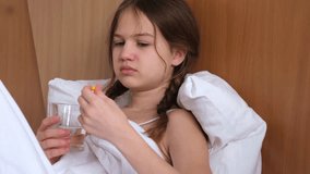 Sick little girl taking medicine and drinking water lying on bed at home, close up. Domestic treatment of illness, flu and cold - Powered by Shutterstock - Get 15% off with code: PIKWIZARD15