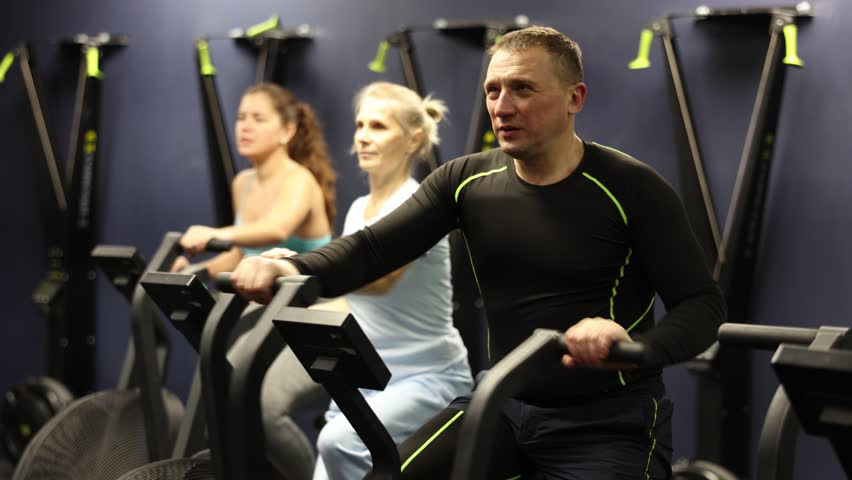 Two sportswomen and one sportsman working out on elliptical machine