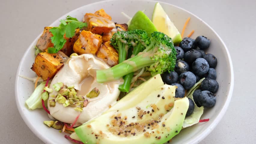 Balanced vegan lunch bowl with baked sweet potato, avocado, berries, salad and hummus. Plant Based Diet Concept.