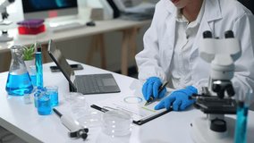 Laboratory technician in white coat and blue gloves analyzing data on tablet and taking notes on clipboard, surrounded by beakers, flasks, and microscope - Powered by Shutterstock - Get 15% off with code: PIKWIZARD15