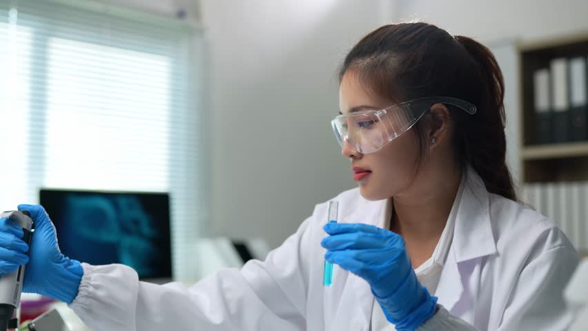 Laboratory technician wearing lab coat, safety glasses and gloves, using a pipette to analyze a blue liquid in a test tube in a modern laboratory - Powered by Shutterstock - Get 15% off with code: PIKWIZARD15