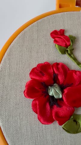 Vertical video of floral hand embroidery with satin ribbons of red poppy flowers in yellow plastic hoop on white background. Crafts and embroidery as hobby and leisure. Top view, close-up, flat lay