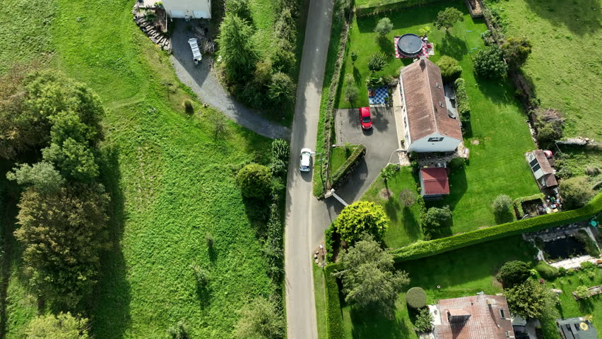 A drone glides above a car cruising along a winding road through the sunny French countryside. It tracks the vehicle, revealing golden fields, lush greenery, and a bright blue sky. Smooth and scenic.
