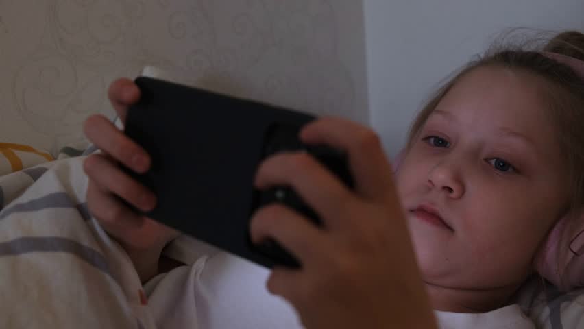 A girl plays an online game on her smartphone at night. Children's dependence on smartphones. Gadget addiction.