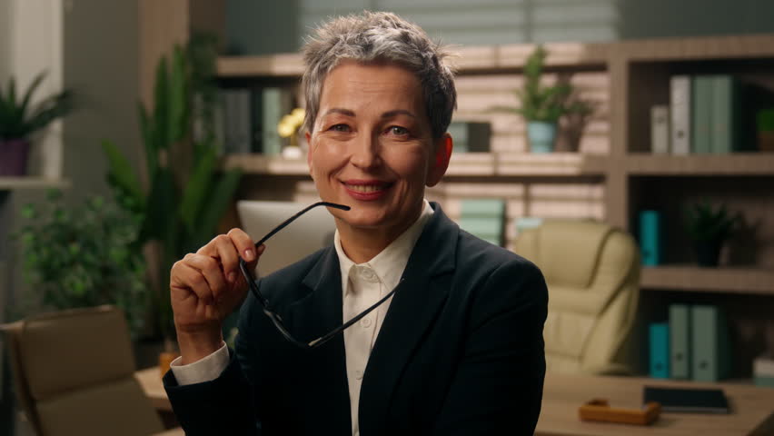 In office pensive thinking thoughtful old Caucasian woman business female businesswoman mature senior employer middle-aged holding eyeglasses smiling come up with idea looking at camera put on glasses