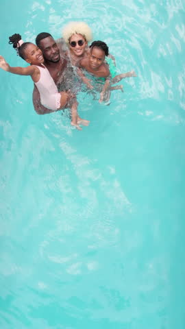 Vertical video: African American family swimming and enjoying time together in home pool. leisure, togetherness, outdoor, bonding, summer, slow motion