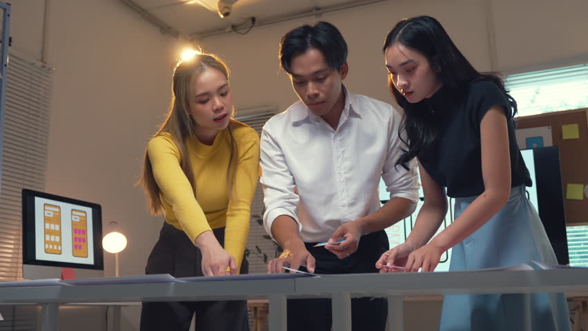 Young Asian uiux developers team working together on a new mobile application prototype, discussing ideas and reviewing design sketches at modern office