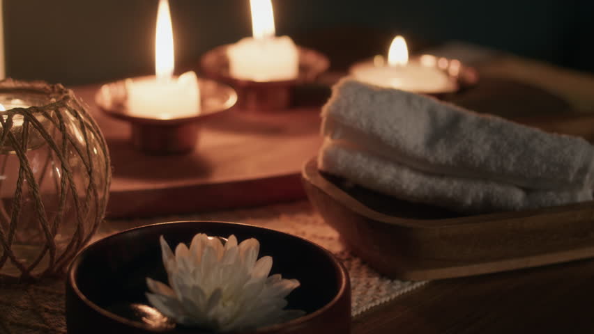 Close-up rack focus view of composition of three candle holders with burning candles, white flower and towel conveying relaxed atmosphere in spa room - Powered by Shutterstock - Get 15% off with code: PIKWIZARD15