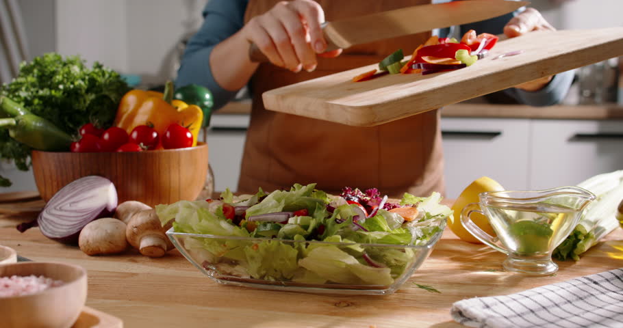 Close-up of Mediterranean salad preparation with fresh vegetables. Female hands chop organic veggies, adding them to a bowl for a vibrant, healthy dish. Clean eating and balanced nutrition showcased