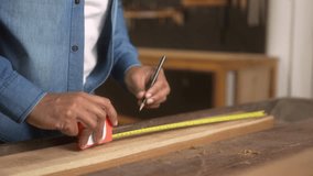 Carpenter measuring wooden plank and marking it with a pencil in workshop. Hands of a craftsman using tape measure on wood while working on precision task - Powered by Shutterstock - Get 15% off with code: PIKWIZARD15