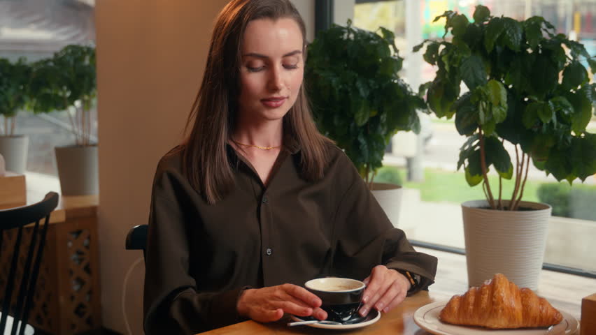 Happy smiling relaxed Caucasian woman girl female business businesswoman lady indoors in cafe in cafeteria restaurant drinking aroma coffee tea drink beverage breakfast lunch croissant smile at camera