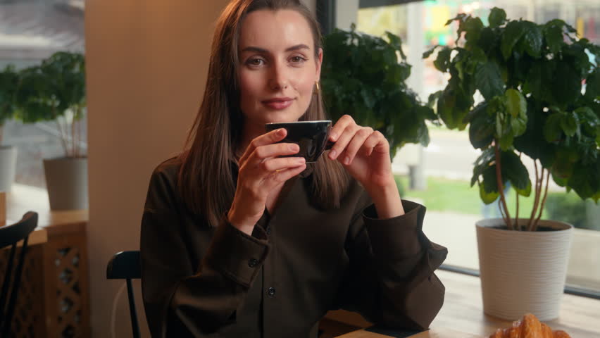 Happy smiling relaxed Caucasian woman girl female business businesswoman lady indoors in cafe in cafeteria restaurant drinking aroma coffee tea drink beverage breakfast lunch croissant smile at camera