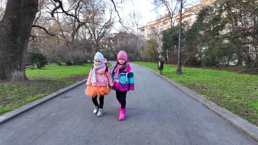 Two girls walking in the park in winter. Two sisters with school backpacks going to school