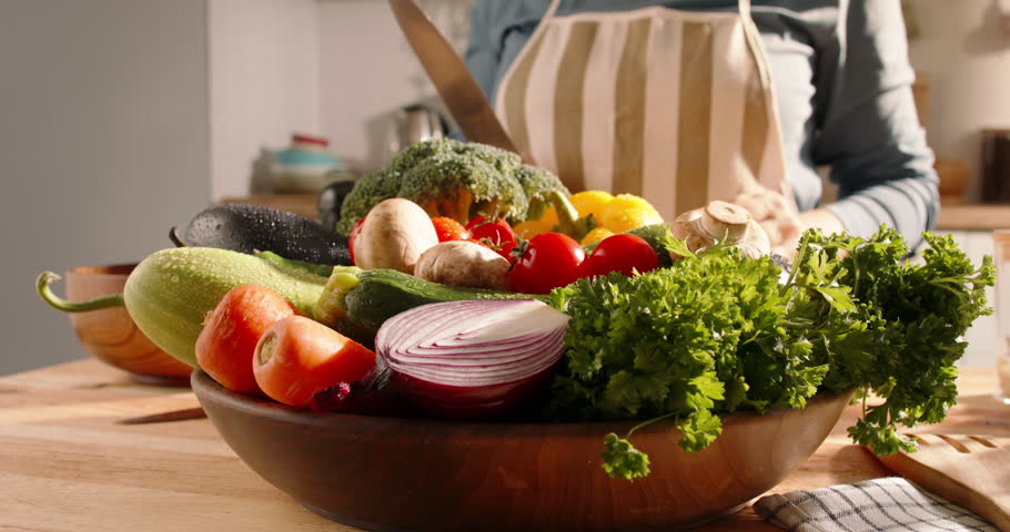 A woman's hand takes a red onion from a wooden plate full of fresh colorful vegetables and begins to prepare a salad. Healthy lifestyle concept of healthy eating, delicious and healthy food