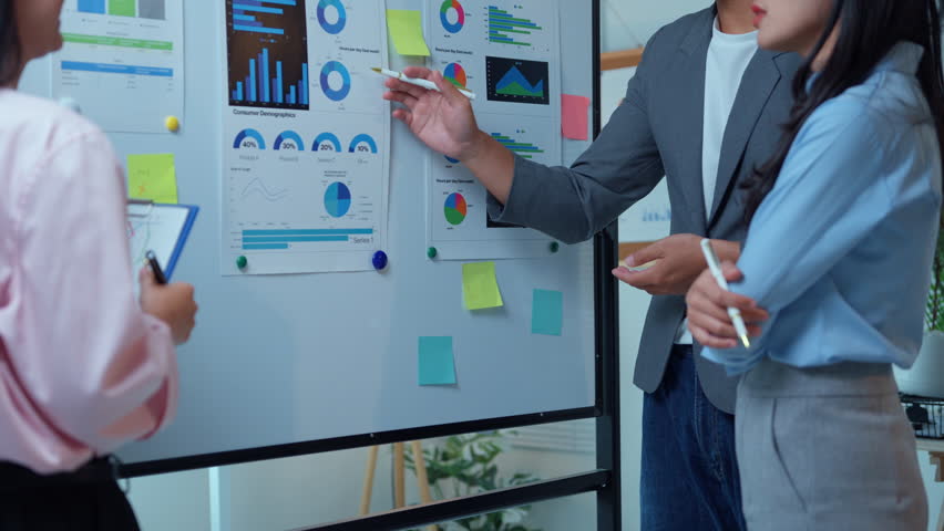 Professional business team analyzing marketing data, collaborating on strategy using whiteboard during collaborative workplace meeting
