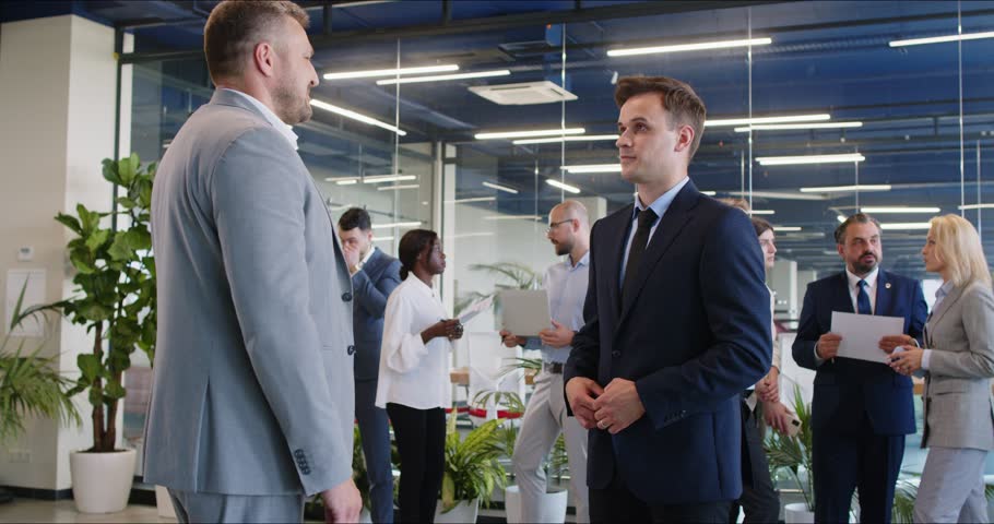 Slow motion video of two cheerful happy business men shaking hands celebrating success making a good deal together standing on a meeting in modern office. Partnership concept. 4k video.