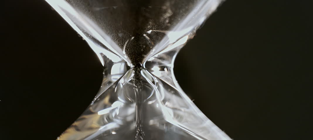 Slow-motion shot of an hourglass with grey sand running out. Transparent sandglass measuring time