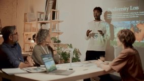 Young African American man standing near projection screen in office, giving presentation and discussing environmental issues with team of multi-ethnic colleagues during professional meeting - Powered by Shutterstock - Get 15% off with code: PIKWIZARD15