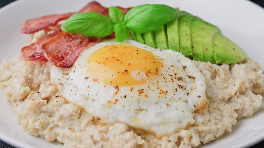 Savory Oatmeal breakfast with egg, bacon and avocado. Tender yolk running out. Healthy food