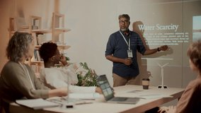 Mature environmental engineer explaining water scarcity issue and renewable energy project to diverse team at professional meeting in office, using projection screen to show presentation slides - Powered by Shutterstock - Get 15% off with code: PIKWIZARD15