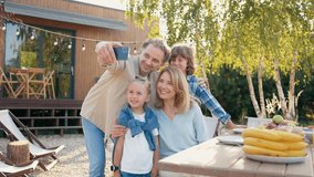 View of Caucasian family gathering together next to table located outside in garden. Father holding smartphone with one hand while trying making selfie. Making photos from different positions. - Powered by Shutterstock - Get 15% off with code: PIKWIZARD15