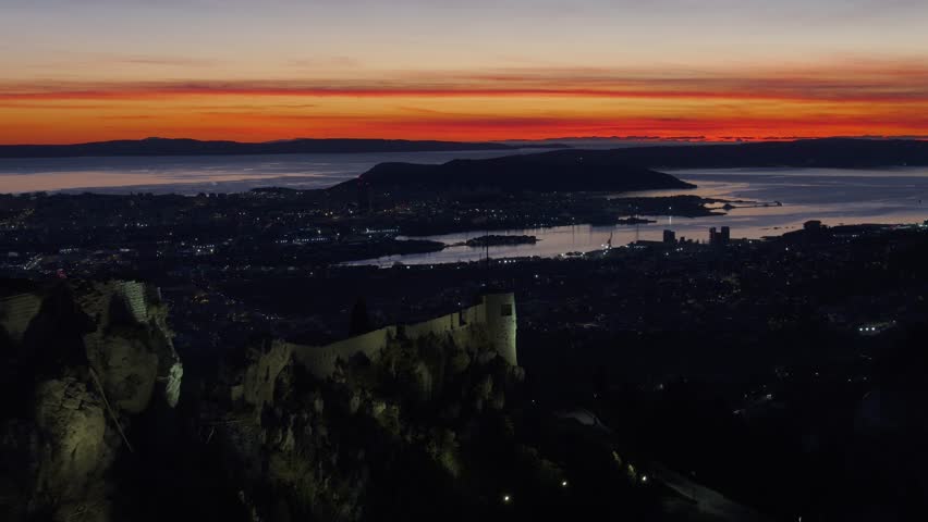 A breathtaking aerial shot of Klis Fortress surrounded by vibrant sunset colors. Split city and the Adriatic Sea in the distance complete this picturesque view of Croatia’s Dalmatian coast.