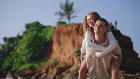 Happy husband carrying wife piggyback, running barefoot on tropical sandy beach. Smiling man and woman having fun at the ocean shore. Newlyweds enjoying honeymoon on the paradise island. - Powered by Shutterstock - Get 15% off with code: PIKWIZARD15