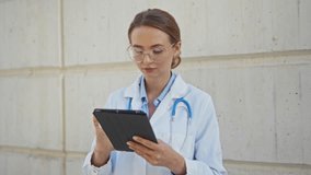 Female doctor with stethoscope using tablet outside urban hospital building focused on her task. - Powered by Shutterstock - Get 15% off with code: PIKWIZARD15