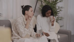 Female friends enjoying relaxing home spa day, applying pink clay masks while sitting comfortably on sofa, sharing wellness moment with skincare routine and cheerful mood - Powered by Shutterstock - Get 15% off with code: PIKWIZARD15