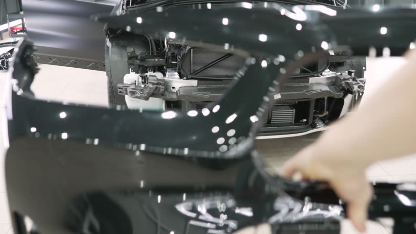 Professional car mechanic carefully removing paint protection film, revealing pristine surface of new black car bumper during detailed automotive service
