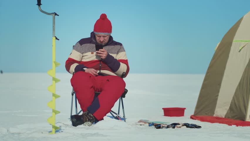 A man finds enjoyment in ice fishing amidst a tranquil, snowy landscape that showcases winter leisure activities