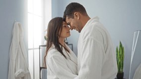 Couple embracing at spa center in white robes showing love and affection in serene indoor setting with large window, potted plant, and hanging bathrobes suggesting relaxation and wellness - Powered by Shutterstock - Get 15% off with code: PIKWIZARD15
