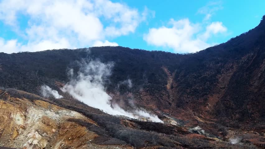 A volcanic mountain in Owakudani, Hakone with steam vents under a bright sky