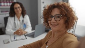 Middle-aged hispanic woman taking selfie with female doctor in clinic office highlights a healthcare setting and patient-doctor interaction. - Powered by Shutterstock - Get 15% off with code: PIKWIZARD15